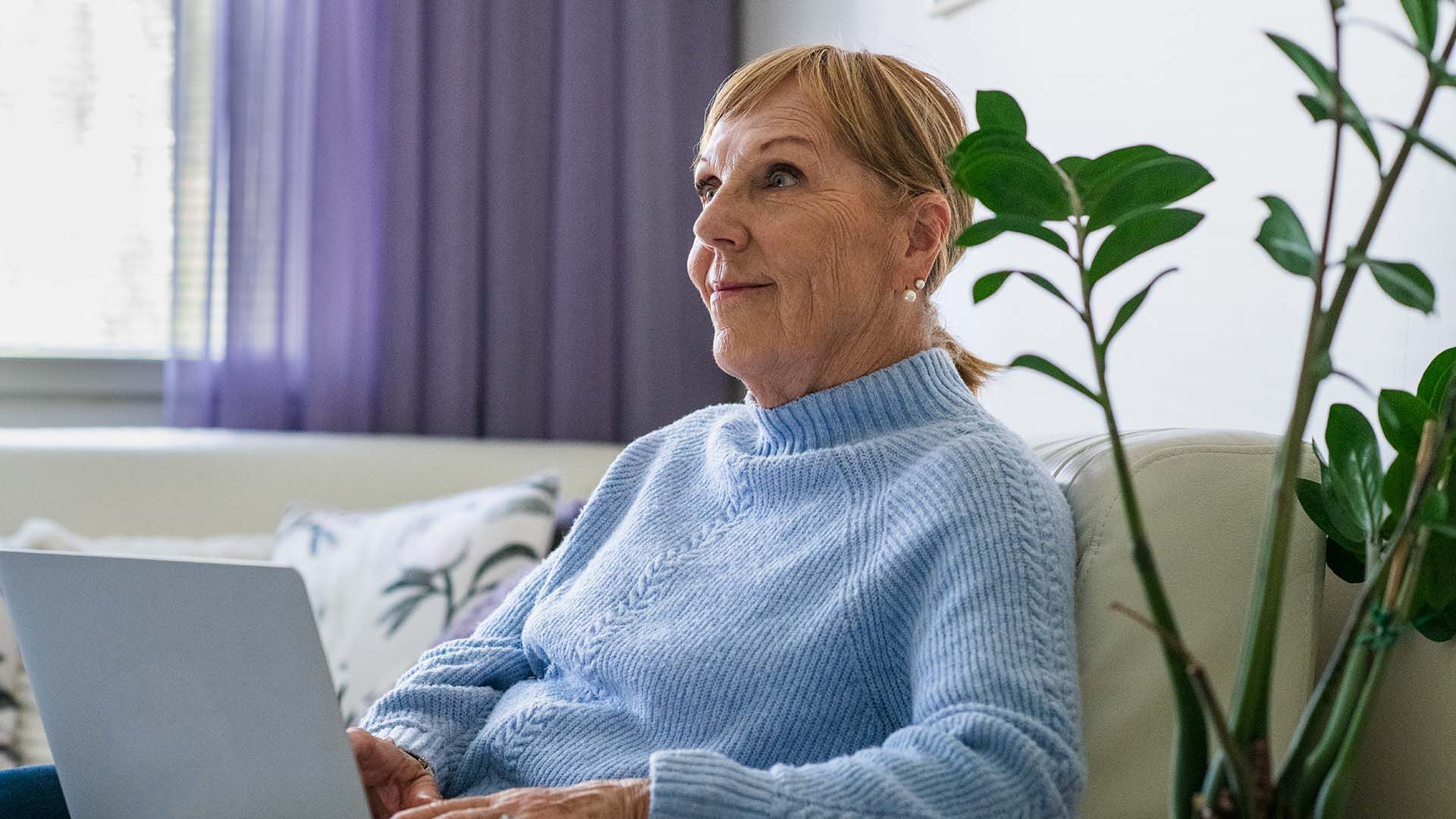 Rouva istuu sohvalla tietokone syliss&auml;&auml;n 